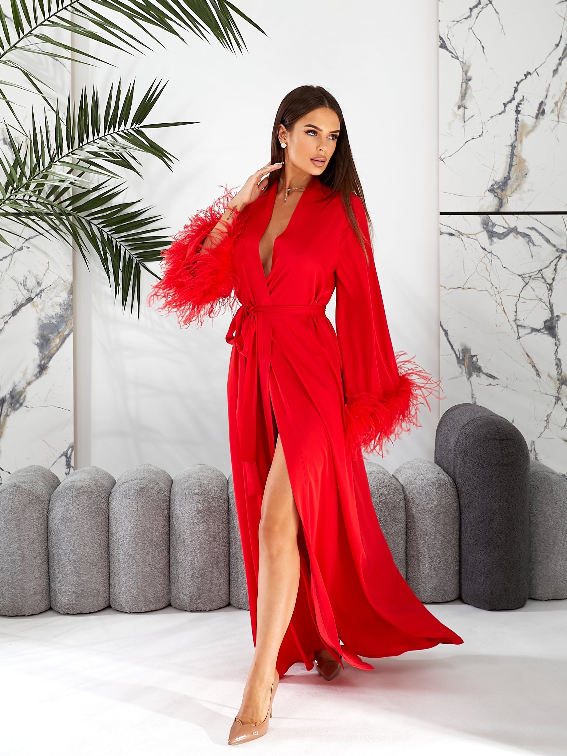Bridal robe silk  Woman in a red dress with feathered sleeves standing in a stylish interior setting.