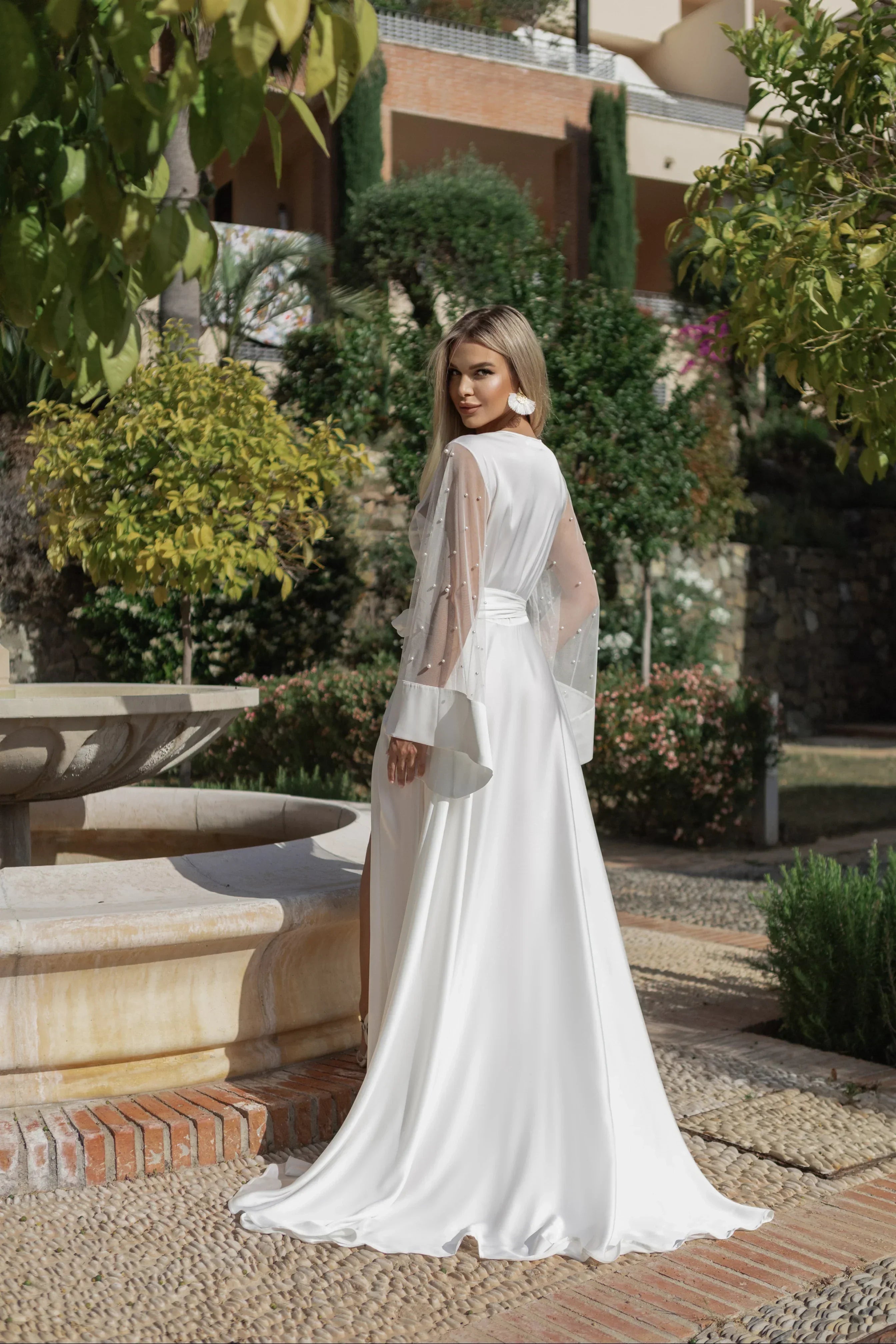 Bride in white silk bridal robe with sheer pearl sleeves, outdoors on wedding morning
