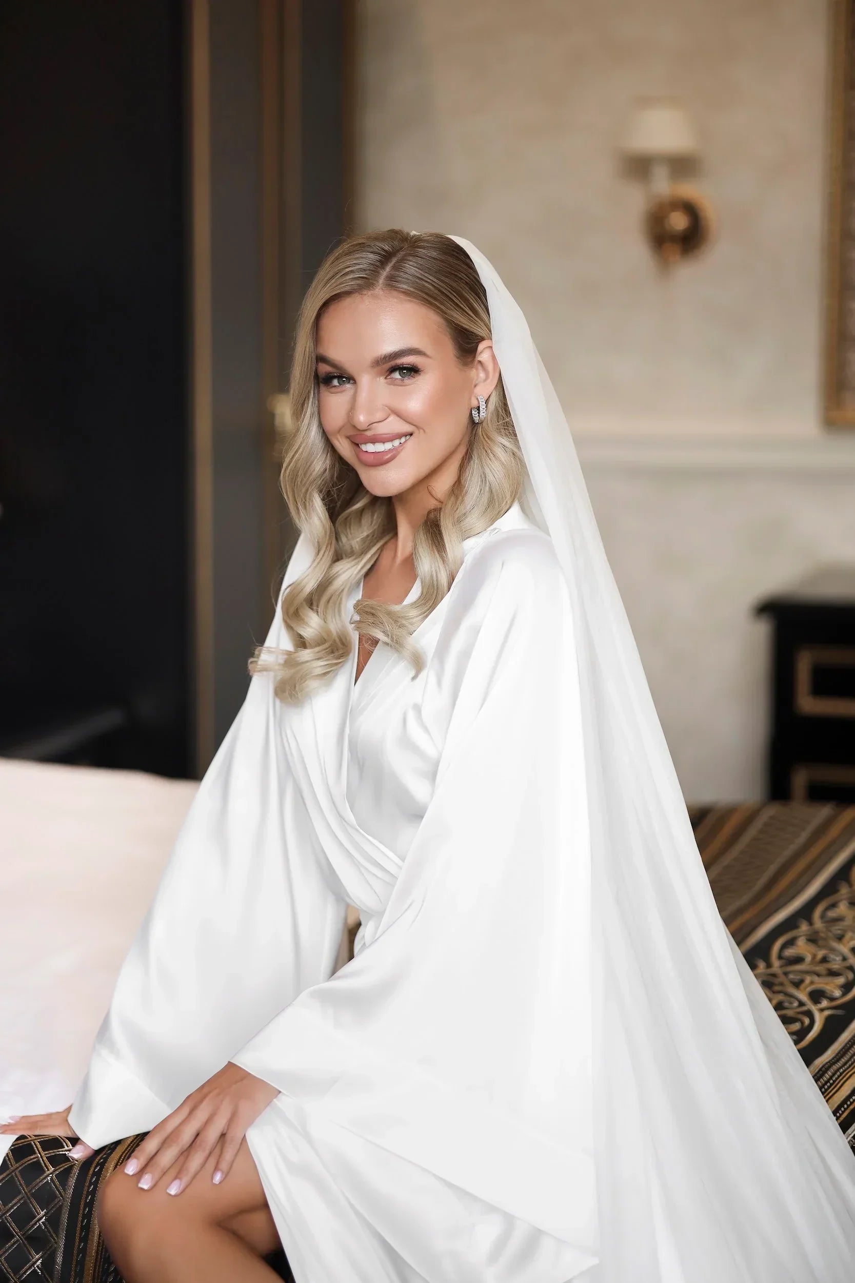 Bride wearing white silk bridal robe with long sleeves, perfect for wedding morning photos.