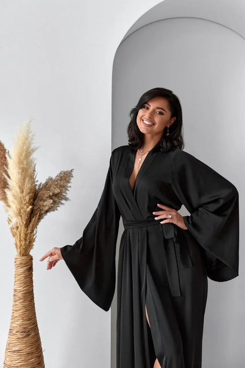 Woman in long black silk bridal robe with wide sleeves, perfect for wedding morning.