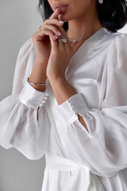 Woman in white silk bridal robe with sheer sleeves, perfect for wedding morning elegance.
